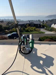 A welding machine with attached cables is positioned on a rooftop, overlooking a suburban neighborhood and a large body of water in the distance.