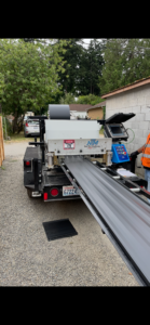 A portable metal panel forming machine mounted on a trailer dispenses long metal sheets onto the ground at an outdoor worksite.
